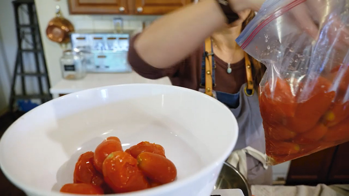 A woman adding frozen roma tomatoes to a Weston tomato press.