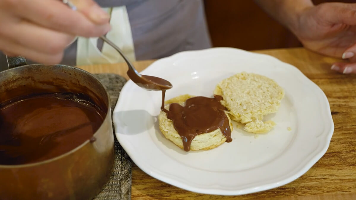 Chocolate gravy being spooned over a flaky buttermilk biscuit.