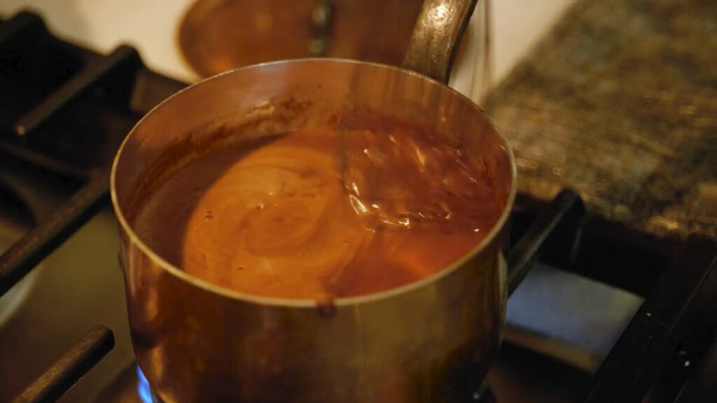 A pot of chocolate gravy on the stove being whisked.
