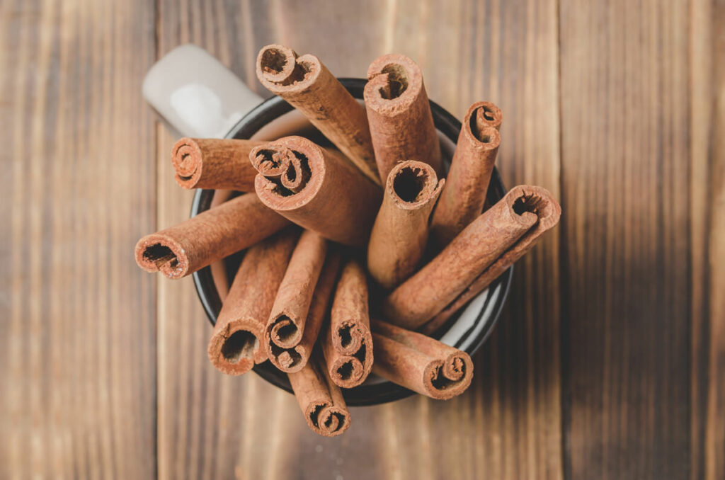Cinnamon sticks in a white mug on a wooden counter.