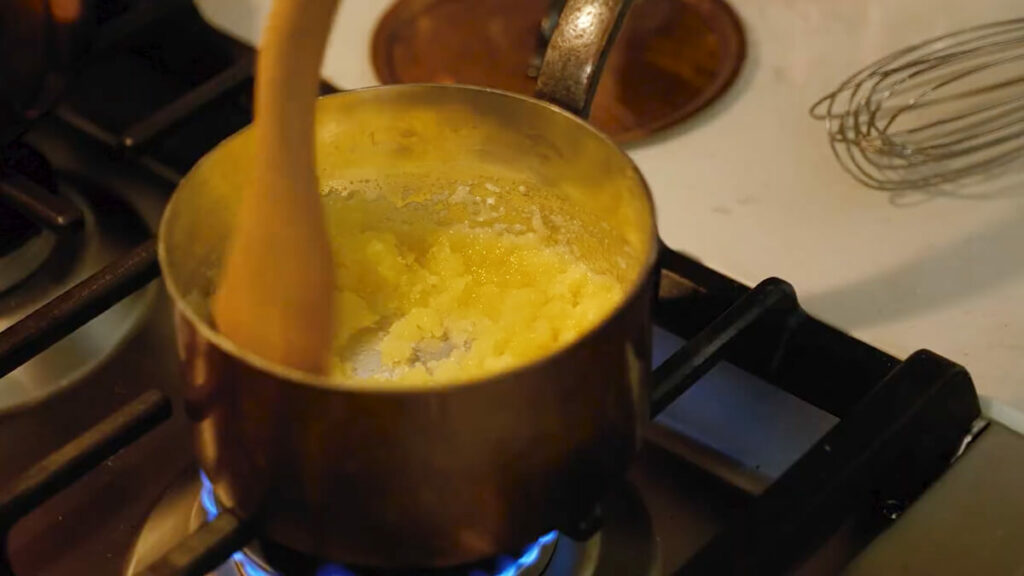A pot of melted butter with flour being stirred on the stove.