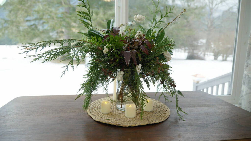 An evergreen bouquet in a wide mouth mason jar on a table by the window.