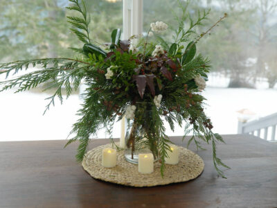 An evergreen bouquet in a wide mouth mason jar on a table by the window.