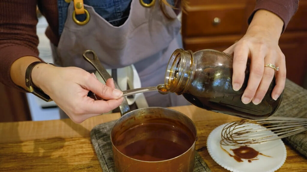 A woman adding vanilla extract to a pot of chocolate gravy.