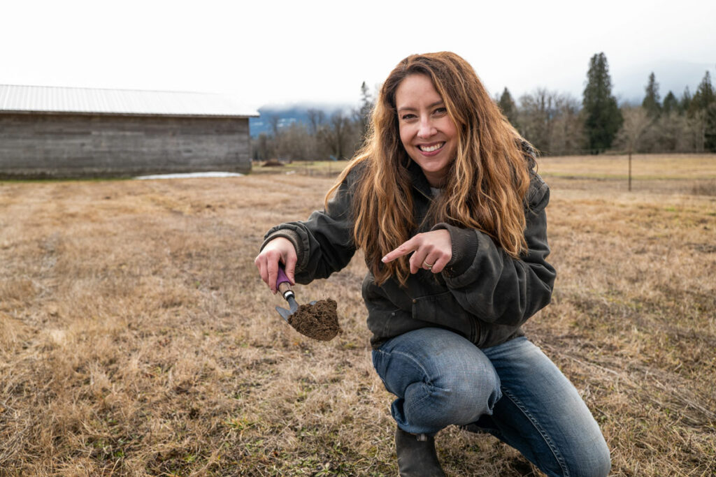 A woman holding up a shovel full of soil.