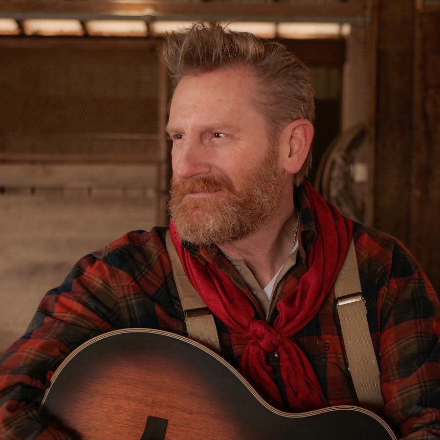 Image of a man in a red and black flannel holding a guitar.