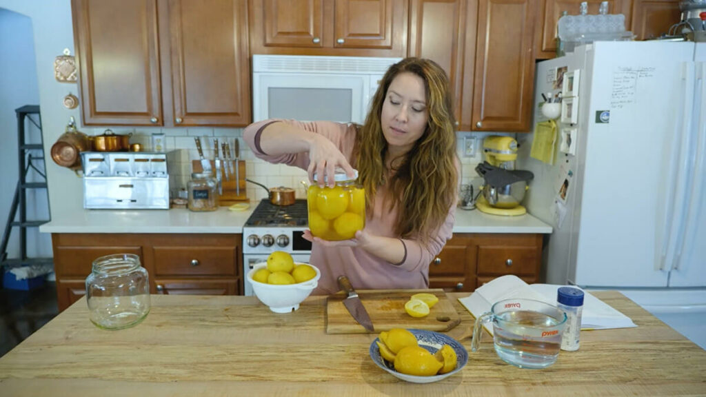 A woman holding up a jar of fermented lemons.