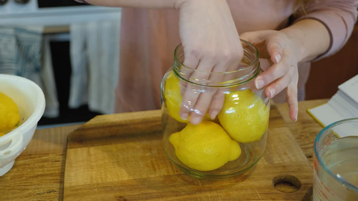 A woman's hands pressing lemons into a jar.