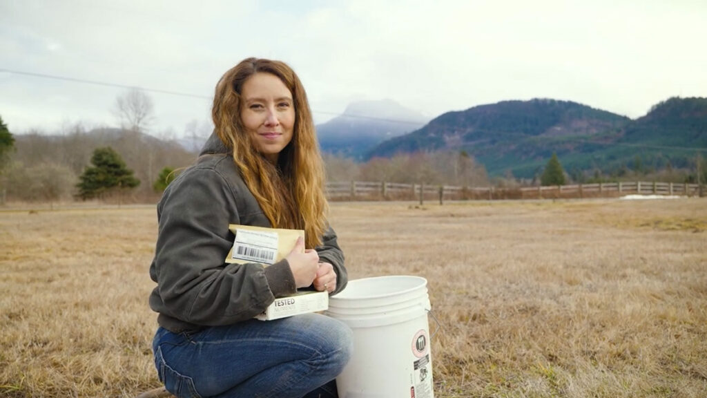 A woman crouching in a field doing a soil test.