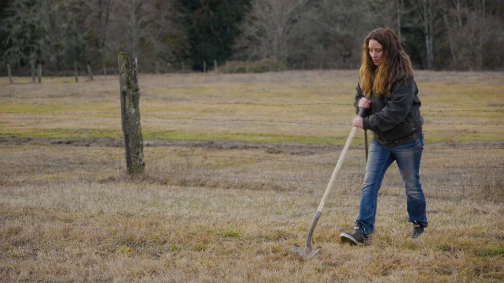 A woman digging up dirt with a shovel.