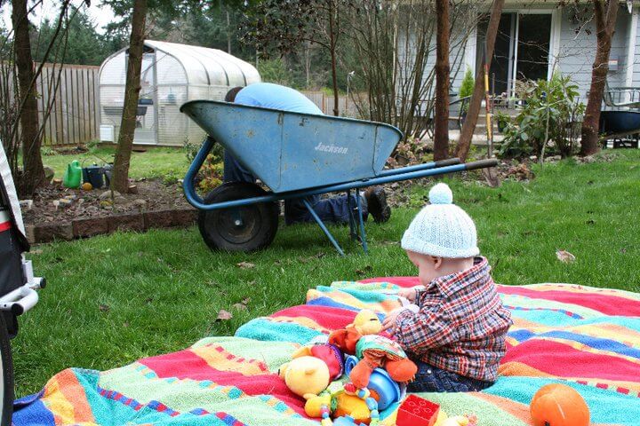 A baby sitting on a blanket in the yard.