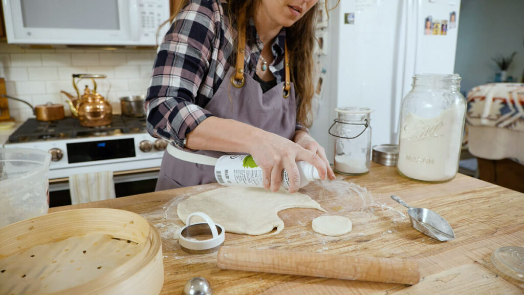 A woman spraying bao bun dough with avocado oil.