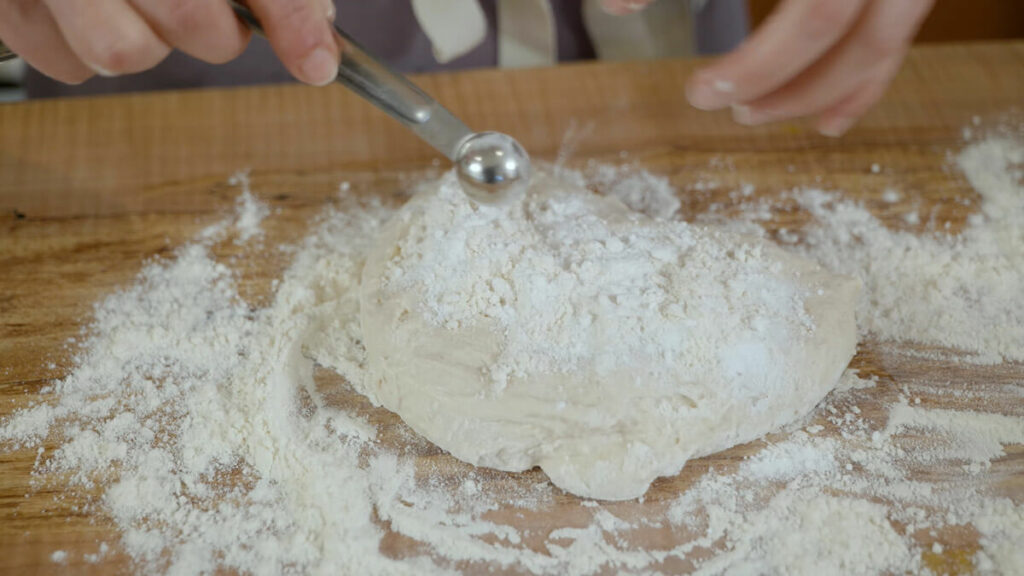 A teaspoon of baking powder being sprinkled onto bao bun dough.