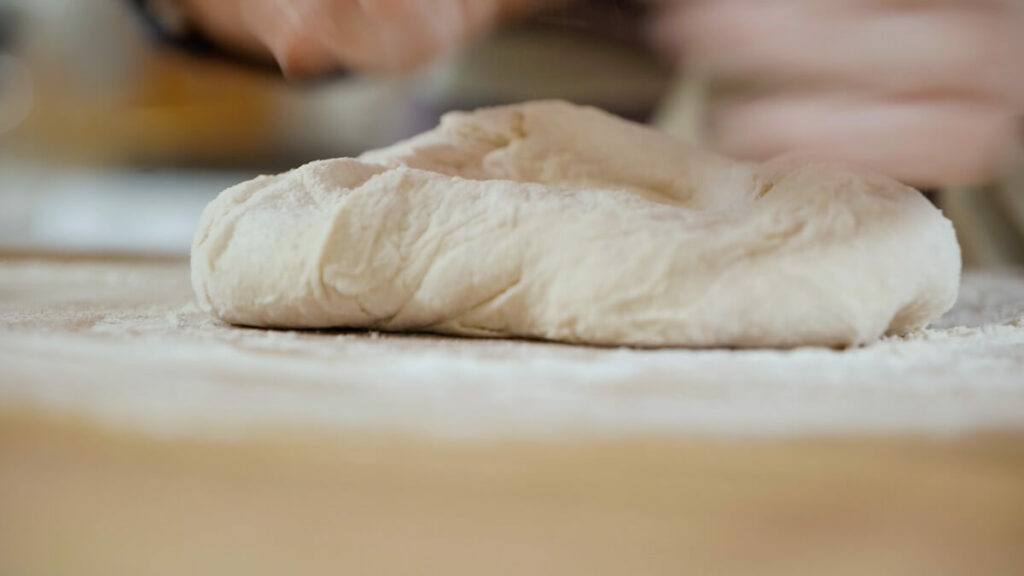 Bread dough being kneaded on a wooden countertop.