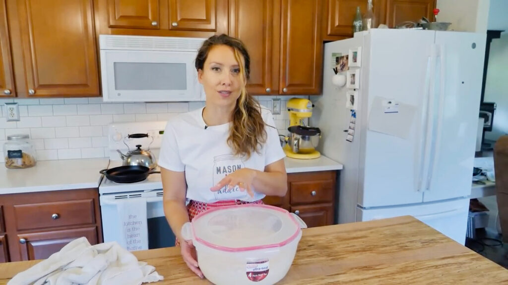 A woman standing behind a covered bowl with bread dough resting inside.
