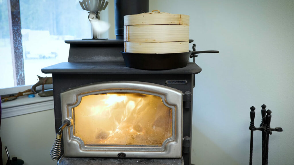 A wooden steamer basket in a cast iron pan on a wood stove.