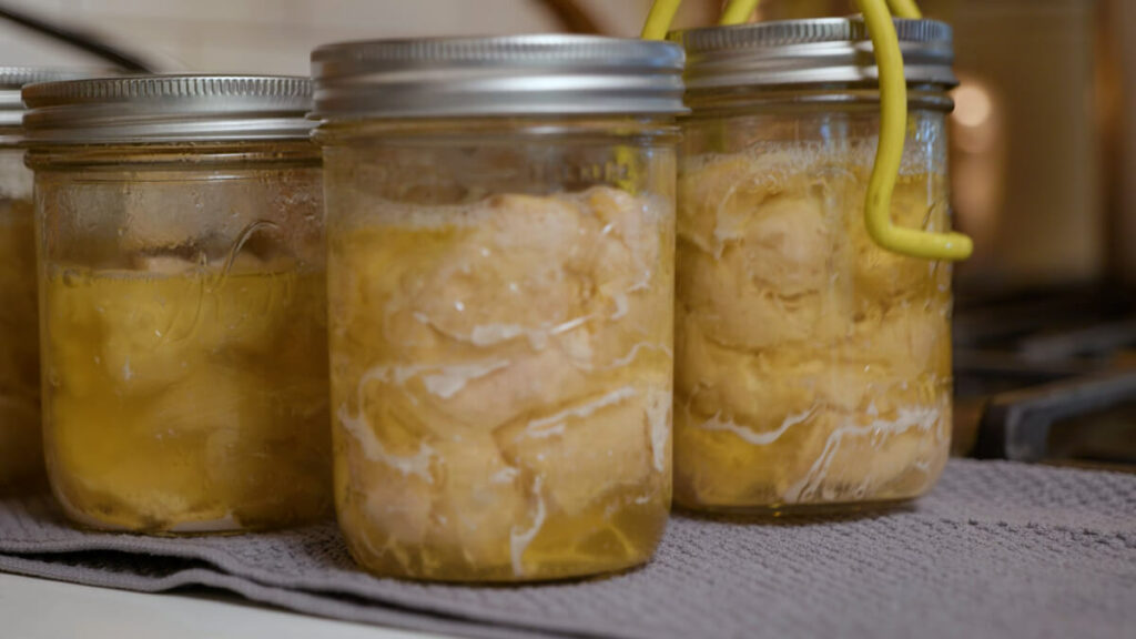 Jars of pressure canned chicken on a towel-lined counter.