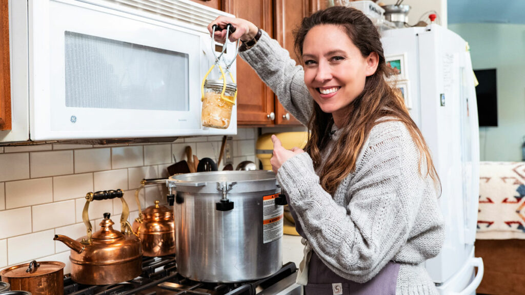 A woman pulling a jar of canned chicken out of a pressure canner.