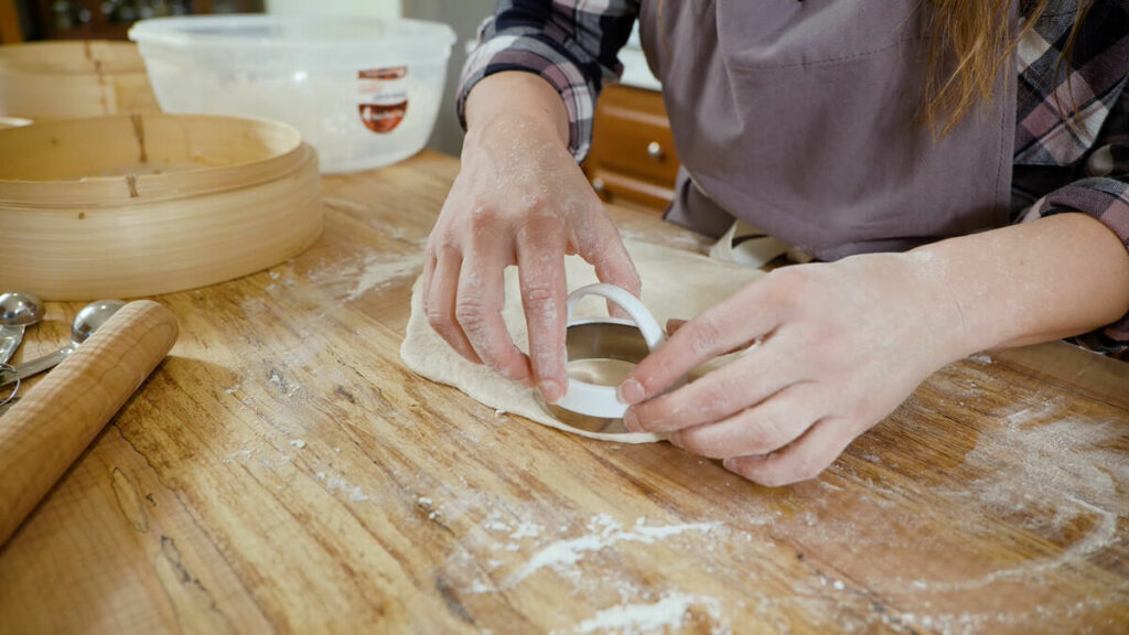 Dough being cut with a biscuit cutter for homemade bao buns.