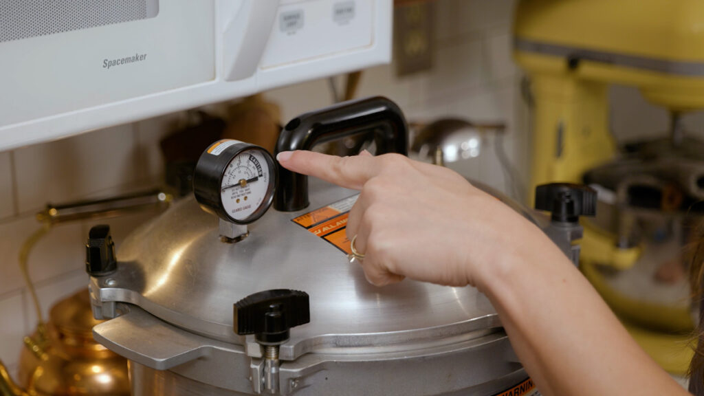 A woman's hand pointing to the pressure gauge on a pressure canner.