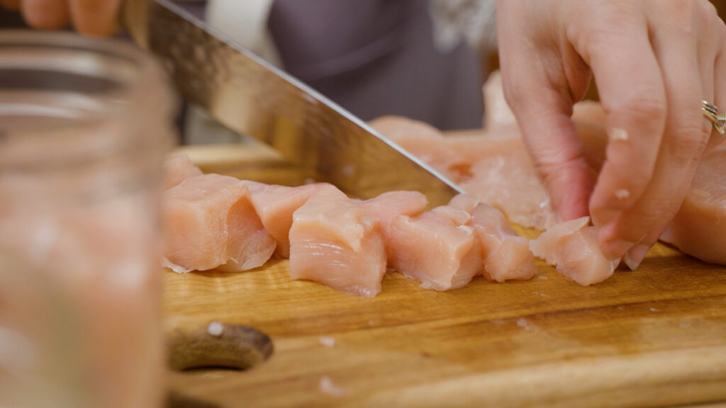 Raw chicken being cubed with a knife.