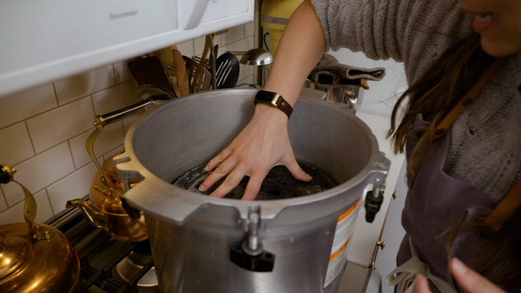 A woman adding a rack between jars of raw packed chicken into a pressure canner.