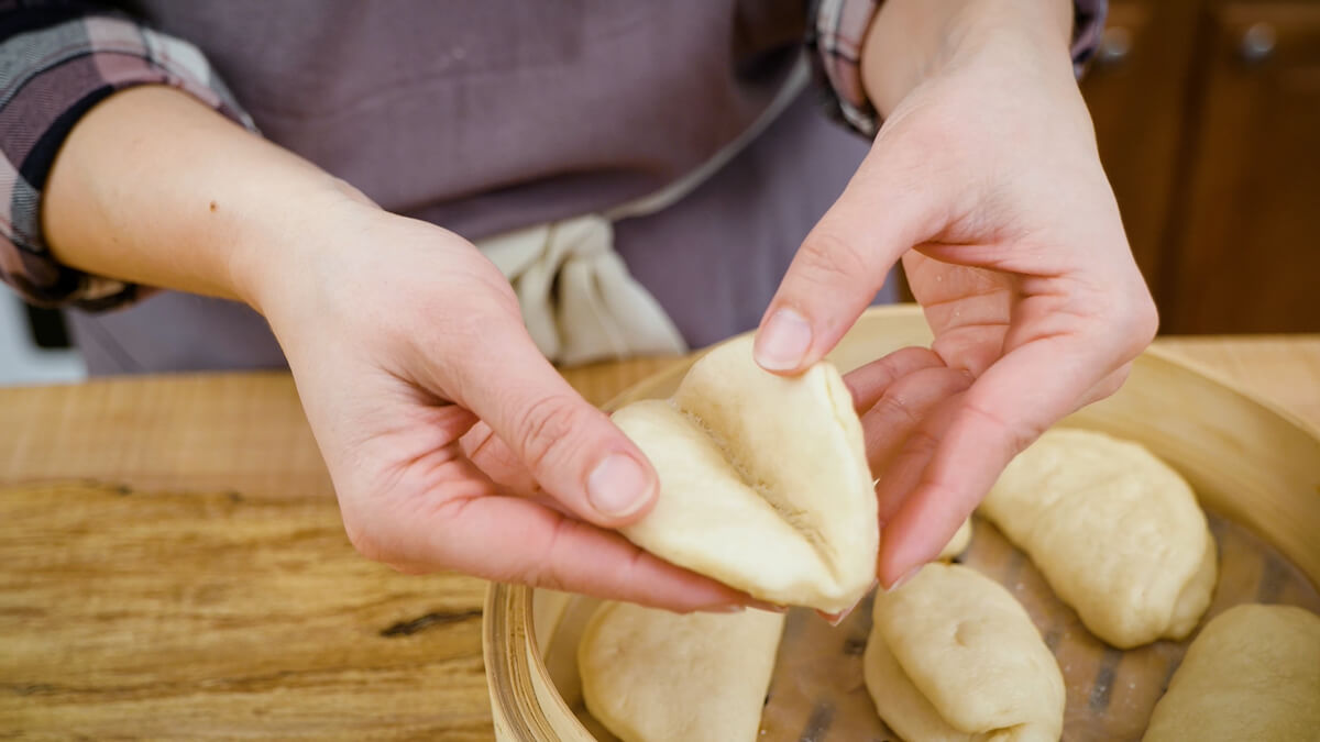 A woman's hands opening a freshly cooked bao bun.