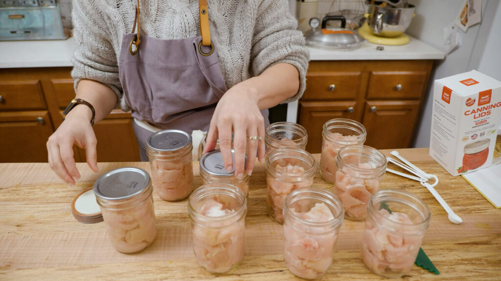 A woman adding canning lids to jars of raw packed chicken.