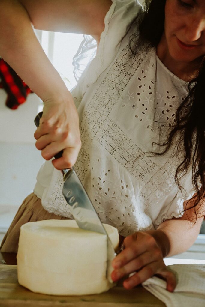 A woman cutting into a wheel of homemade cheese.