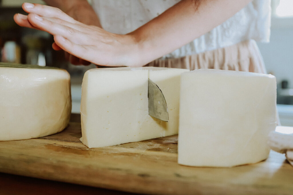 Image of a woman cutting through a large wheel of homemade cheese.