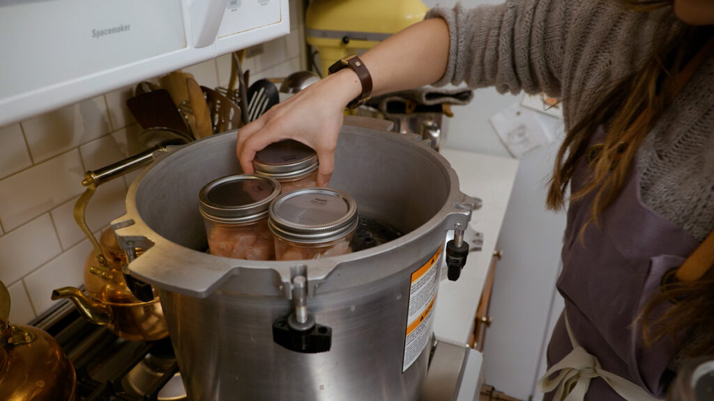 A woman adding raw packed chicken to a pressure canner.