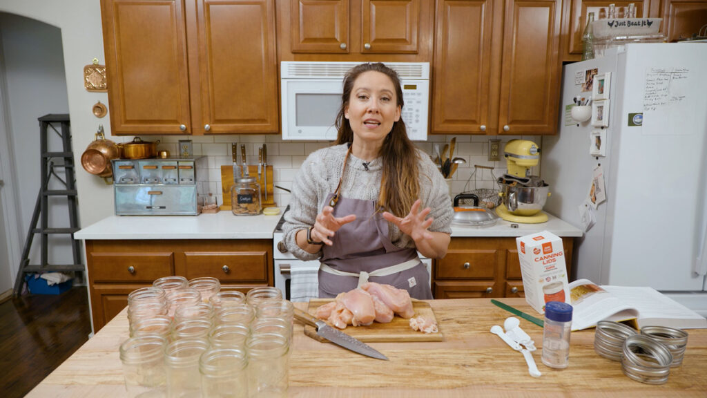 A woman with supplies and ingredients for raw packed pressure canned chicken.