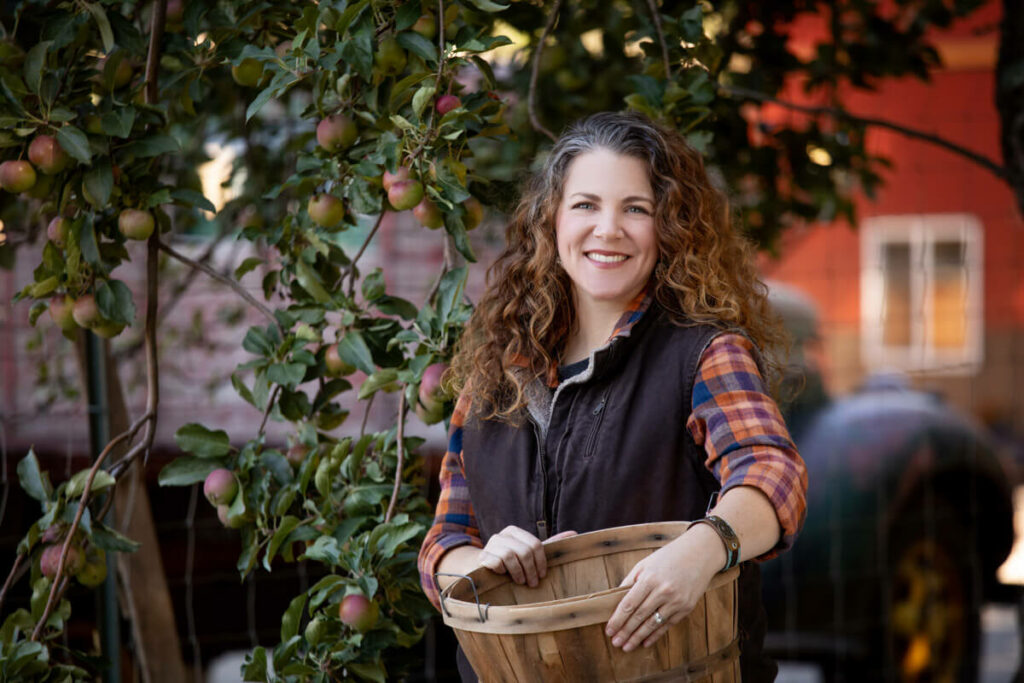 A woman holding a basket for picking apples.