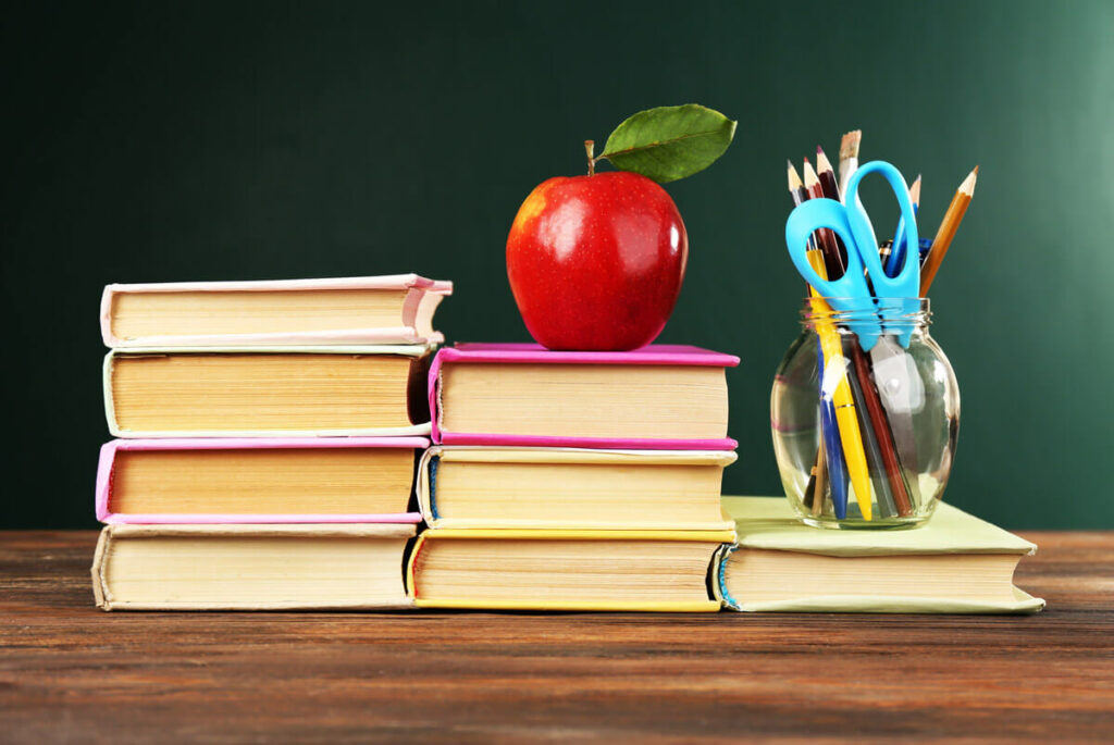 School books on a desk with an apple on top.