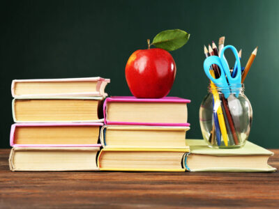 School books on a desk with an apple on top.