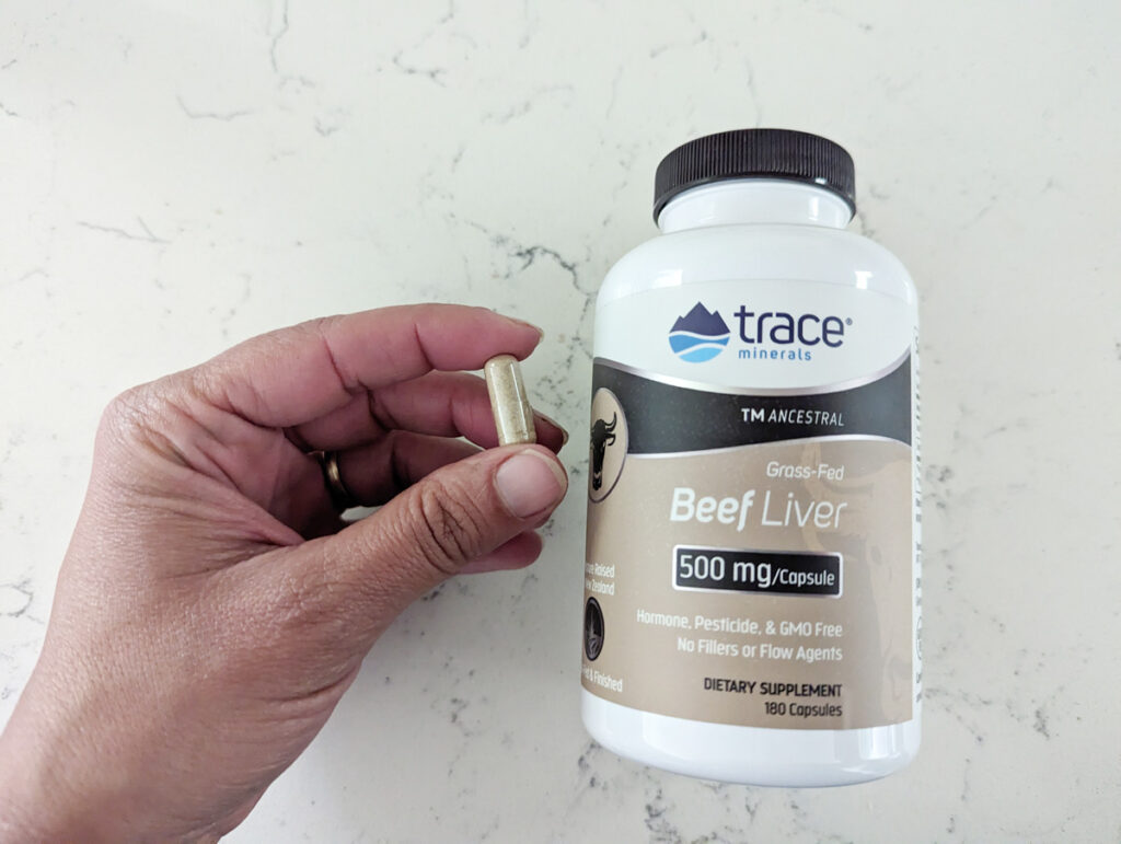 Trace Minerals bottle of beef liver capsules and a woman's hand holding a capsule.