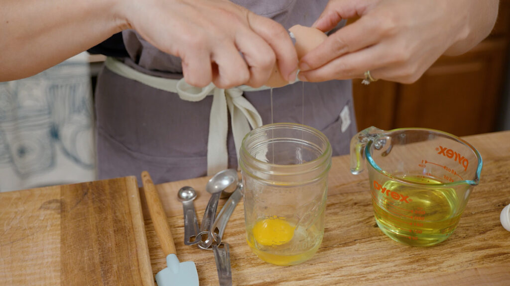 A woman cracking an egg into a Mason jar.