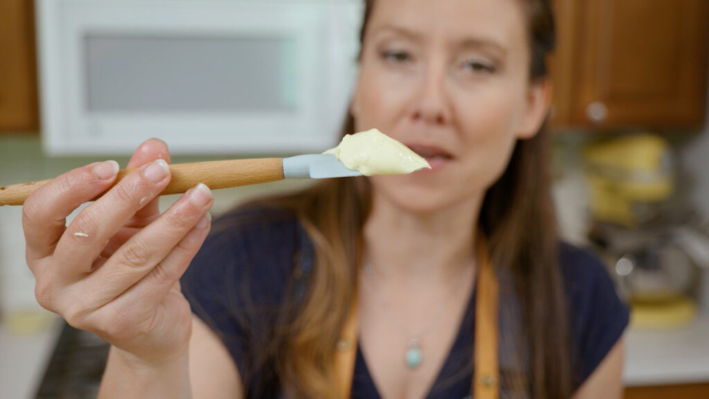 A woman holding up a spatula with homemade mayonnaise on it.