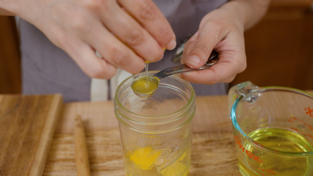 A woman squeezing lemon juice into a measuring spoon.