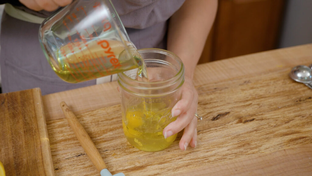 A woman pouring oil into a Mason jar.