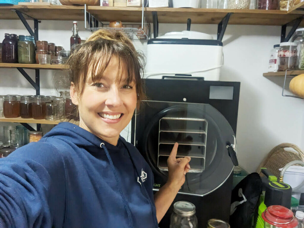 A woman in a pantry pointing to a freeze dryer.