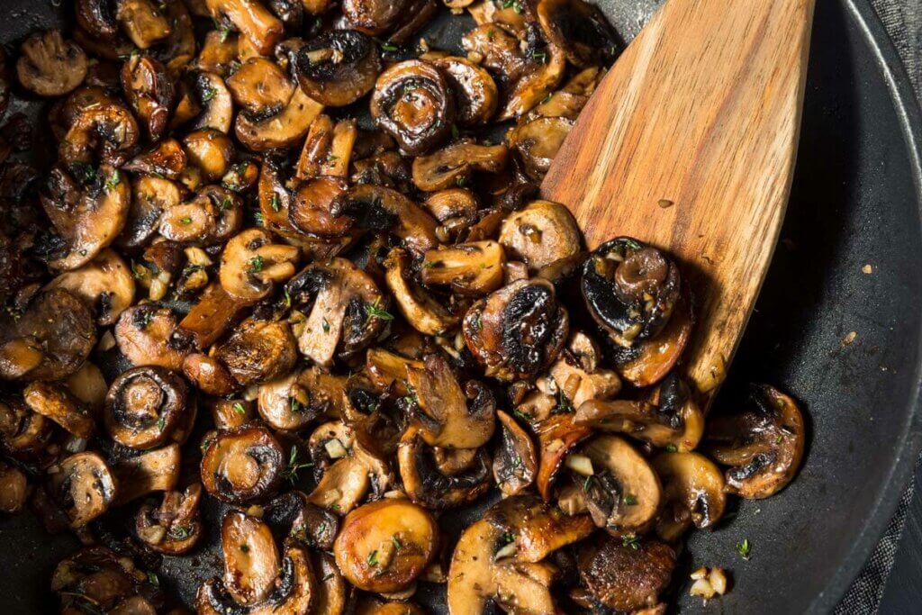 Sauteed mushrooms in a cast iron pan with wooden spatula.