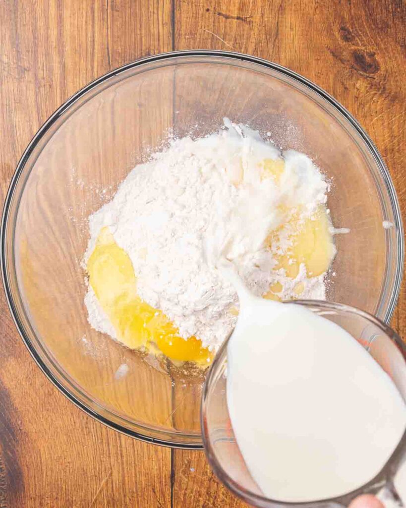 Adding wet ingredients to dry pancake ingredients in a bowl.