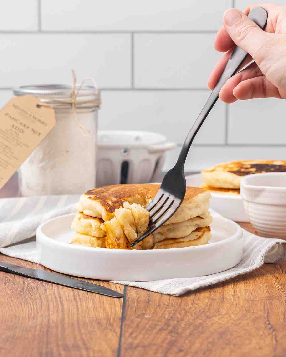 Three pancakes stacked on a white plate with a fork removing a bite to show texture.