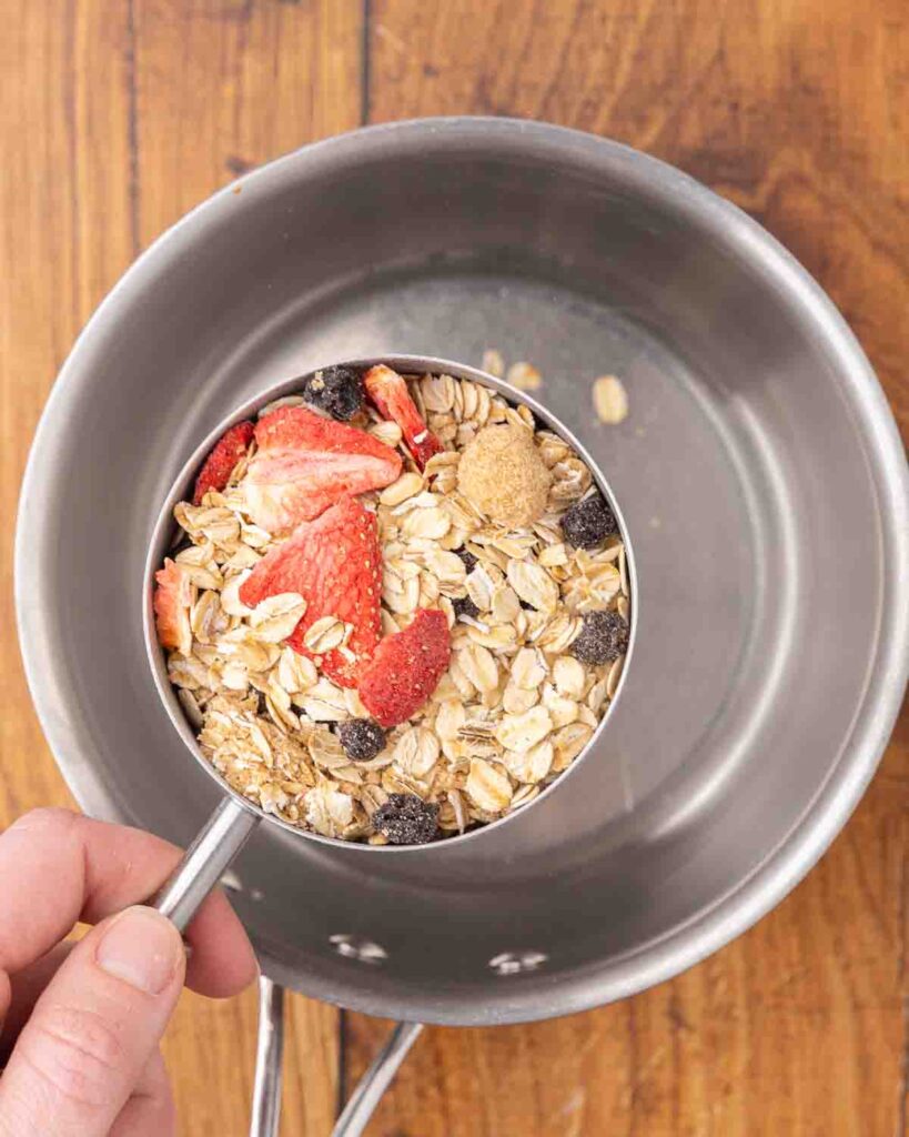 Pouring a cup of instant oatmeal mix into a saucepan.