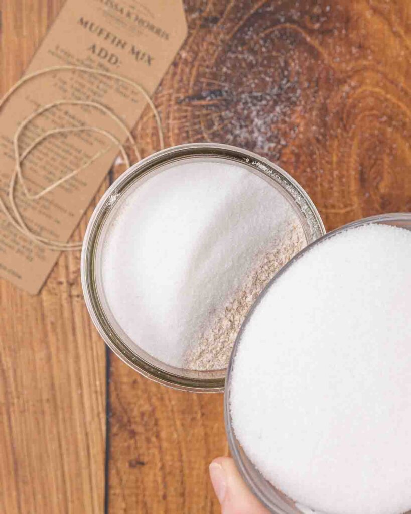 Pouring sugar into a jar filled with muffin mix ingredients.