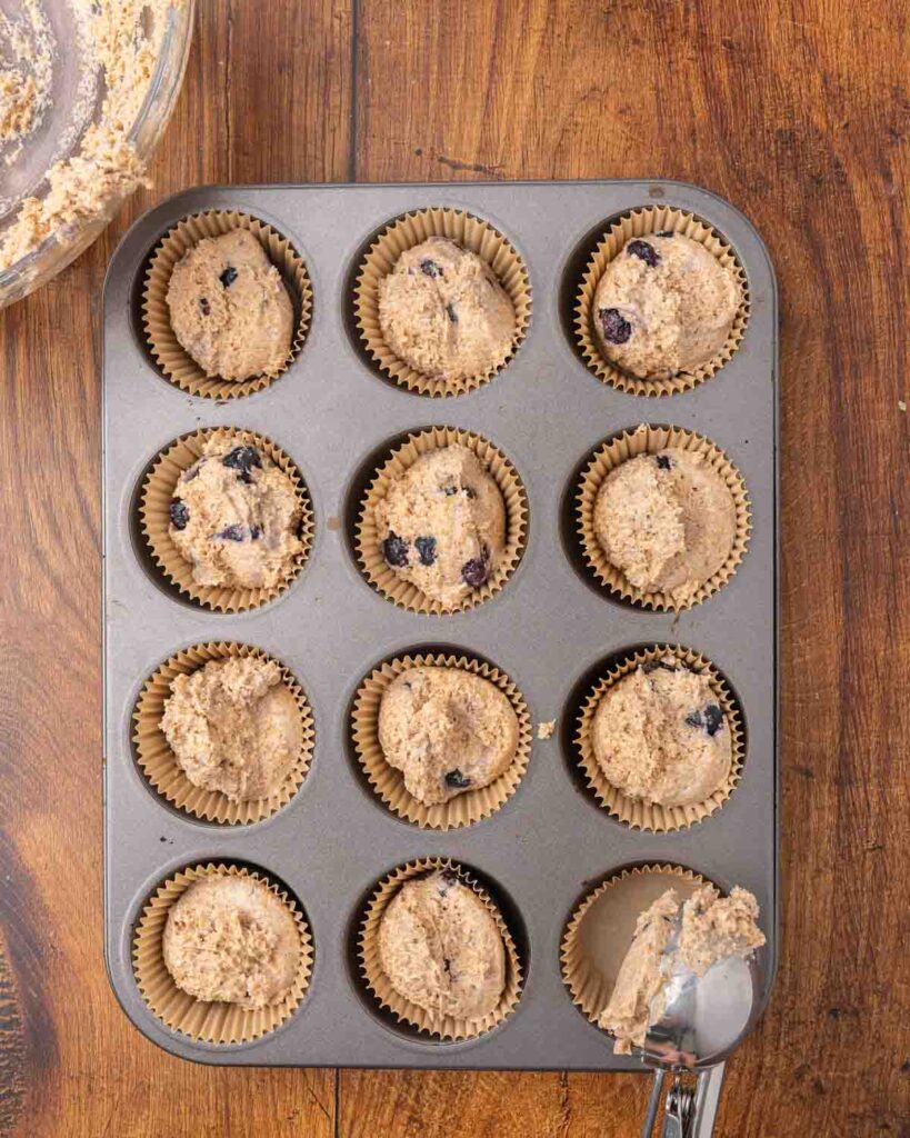 Blueberry muffin batter divided into a muffin tin ready to bake.
