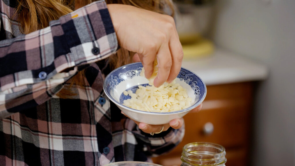 A woman holding up a bowl of beeswax pastilles.