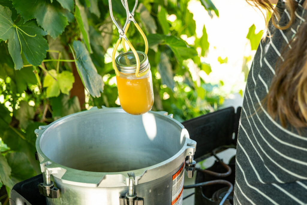 A jar of broth being lifted into a pressure canner.