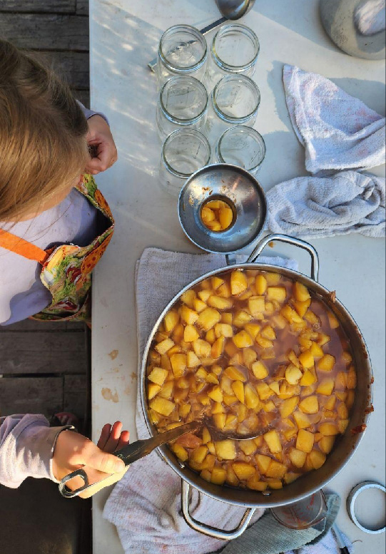 A young girl ladling peaches into canning jars.